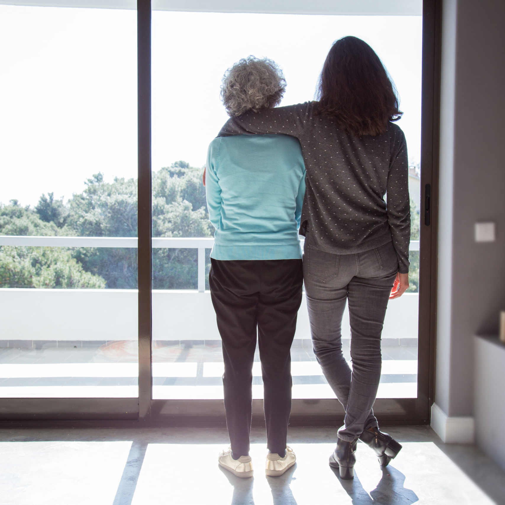 Girl visiting grandma. Back view of young and elderly women standing and looking out window. Family and taking care concept