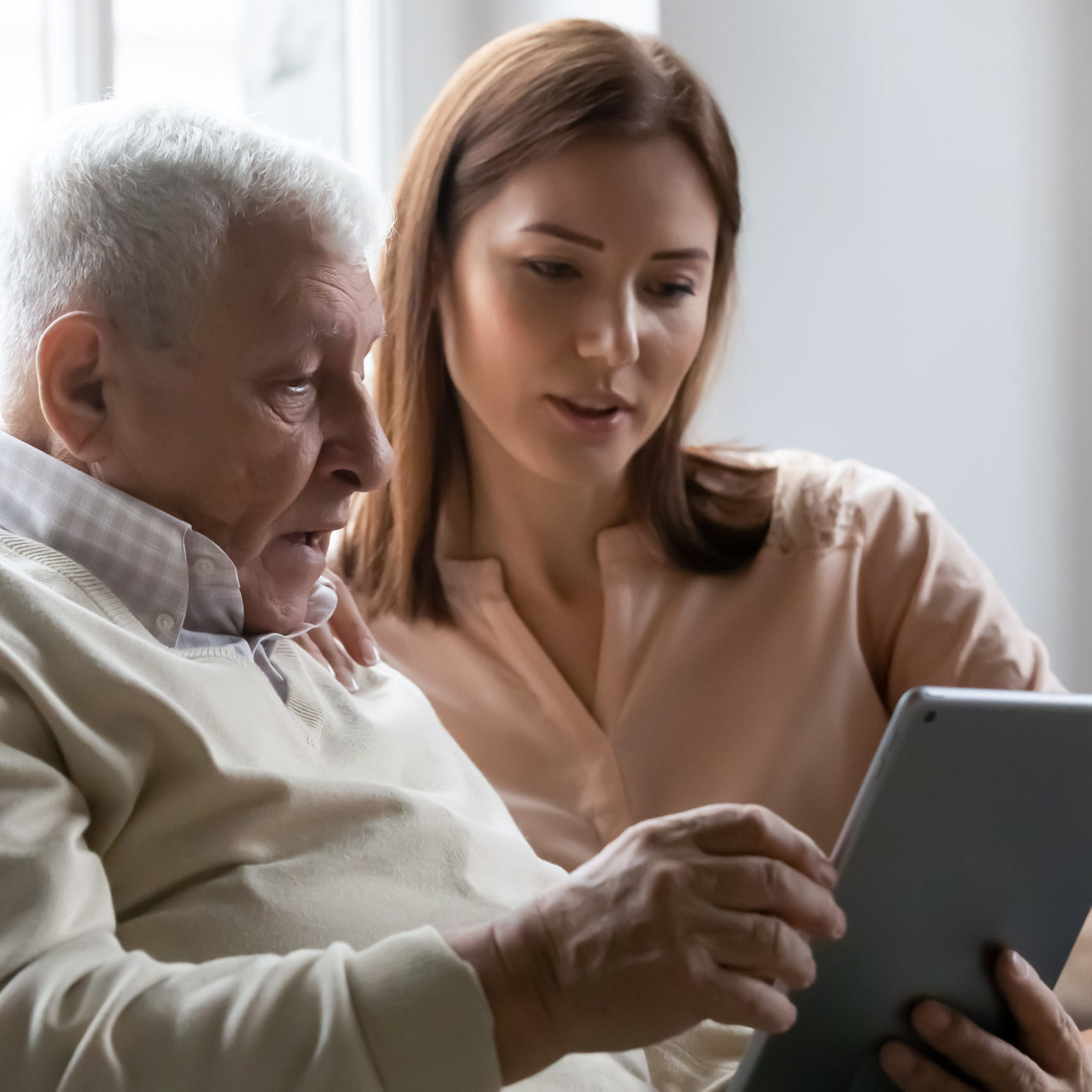 Caring grownup daughter teaching elderly father to use tablet Caring grownup daughter teaching older father to use computer tablet close up, pointing at screen, mature man asking questions about mobile device to young woman, elderly and technology concept